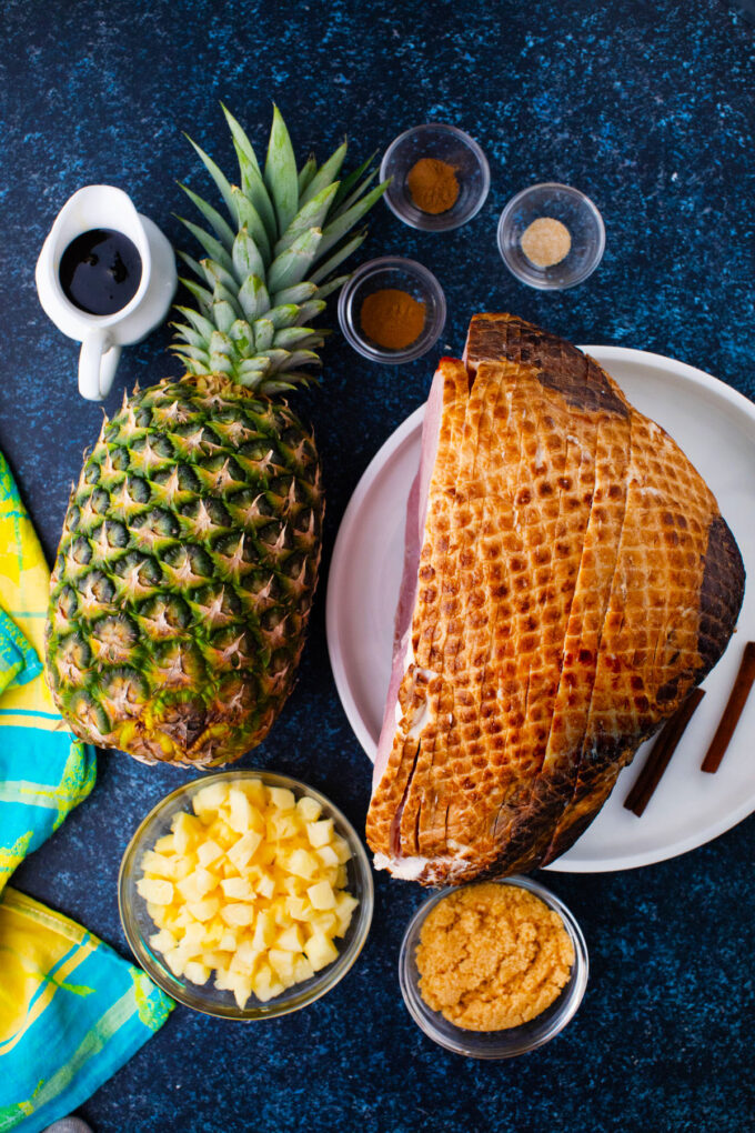 Overhead shot of slow cooker pineapple ham ingredients arranged on a dark table.