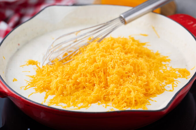 Adding shredded cheddar cheese to creamy sauce.