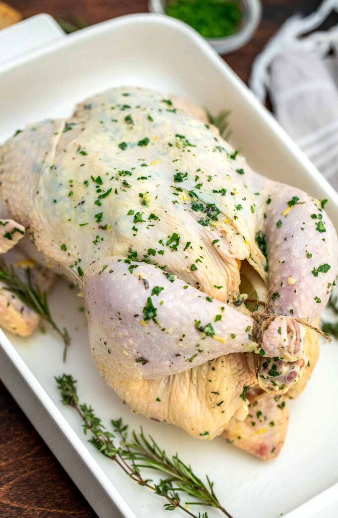 whole chicken covered in garlic butter and herbs in a baking dish.