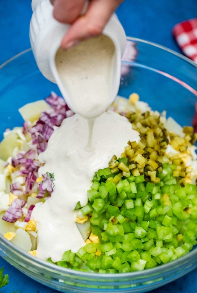 Adding creamy dressing to potato salad with eggs and pickles.