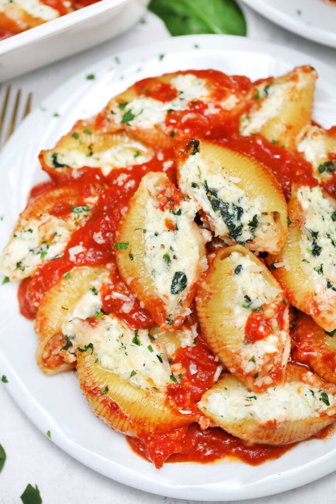 Homemade spinach ricotta stuffed shells with marinara sauce on a white plate.