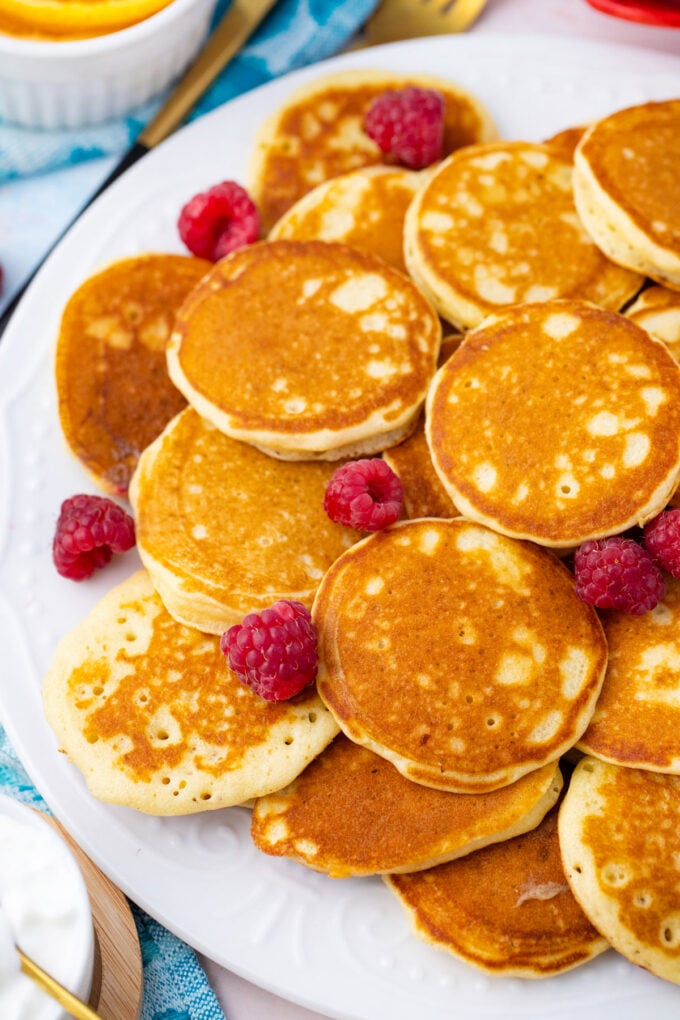 A plate of silver dollars mini pancakes with raspberries.