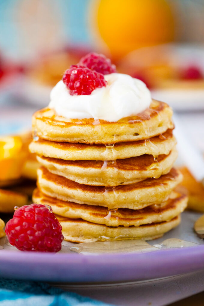 Stack of silver dollars mini pancakes topped with yogurt and fresh raspberries.