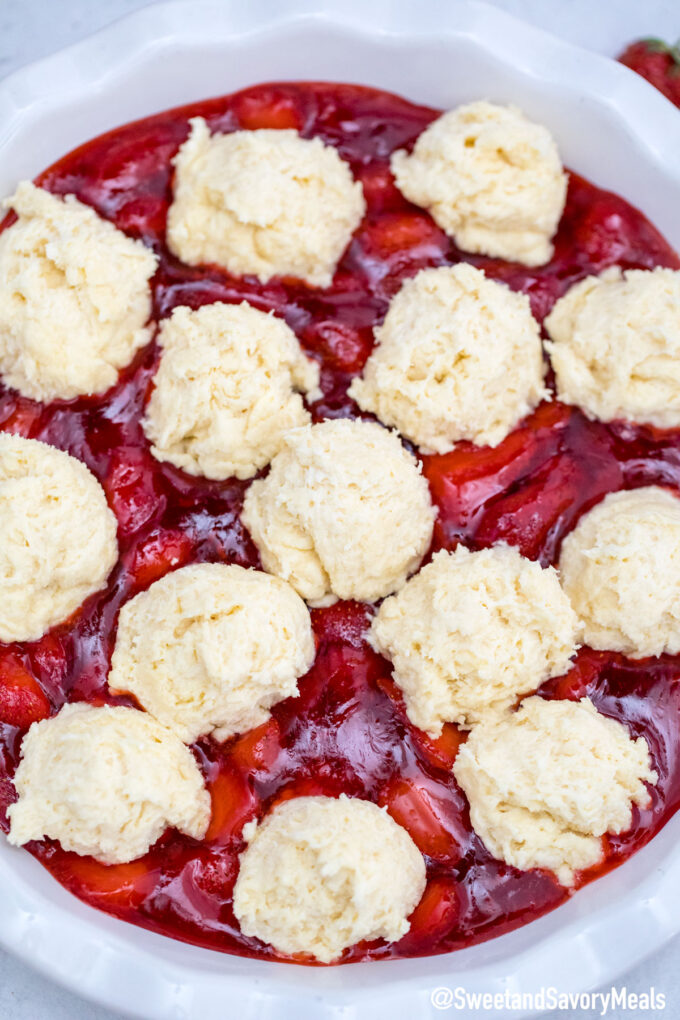 strawberry cobbler filling in a pie dish topped with biscuit dough