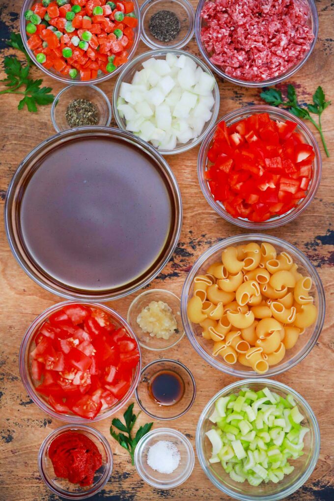 Overhead shot of beef and macaroni soup ingredients in bowls on a wooden table.