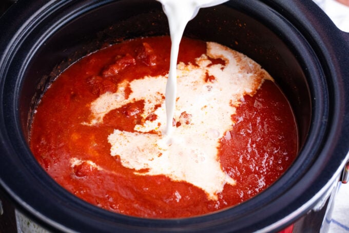 Pouring cream into slow cooker chicken tikka masala.