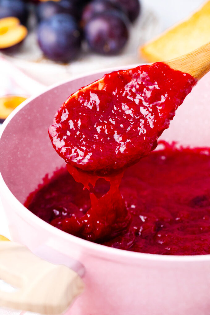 Plum jam dripping of a spoon in a saucepan.