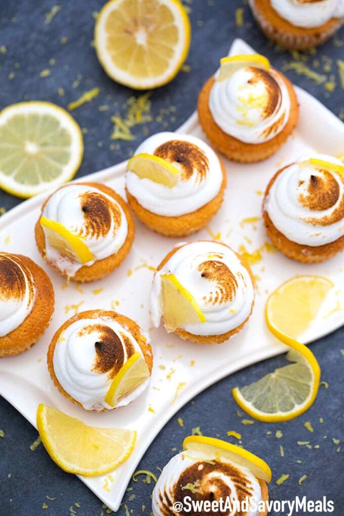 Lemon meringue cupcakes on a white plate with lemons.