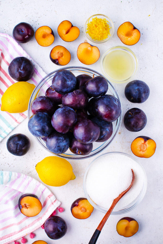 Overhead shot of plum jam ingredients in bowls on a table.