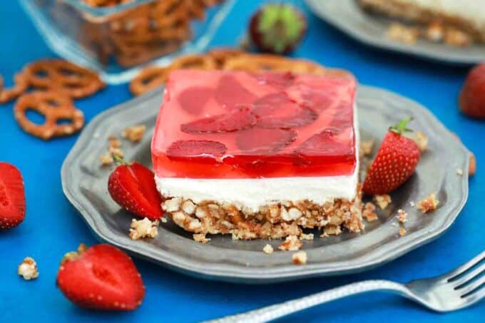 strawberry pretzel salad slice on a plate with fresh strawberries and pretzels in the background