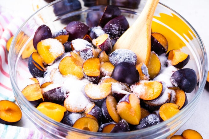 Mixing plums and sugar in a bowl.