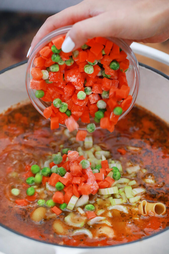 Adding frozen vegetables to beef and macaroni soup.