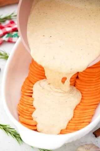pouring creamy sauce on top of thinly sliced sweet potatoes in a baking dish