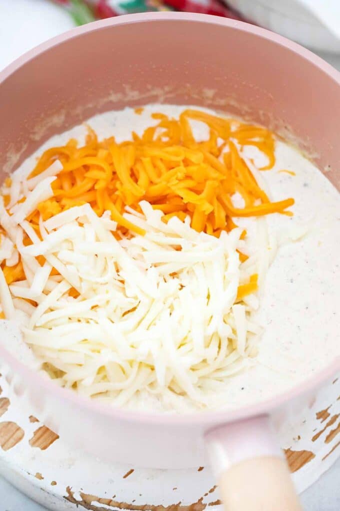 mixing white and cheddar cheese into cream in a saucepan