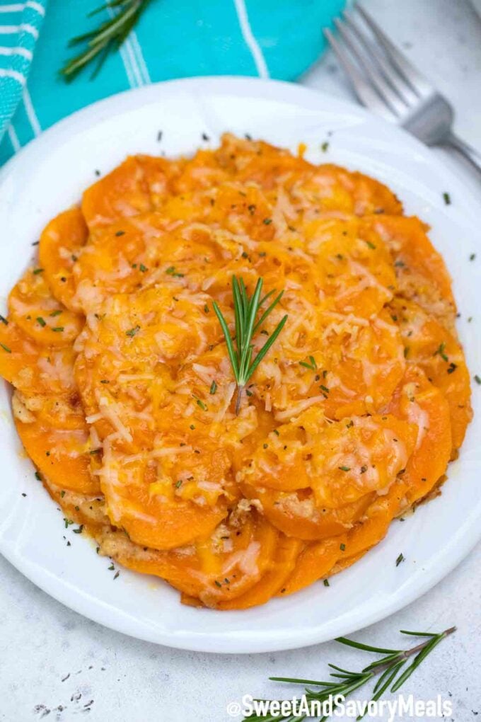 Scalloped sweet potatoes topped with rosemary on a white plate