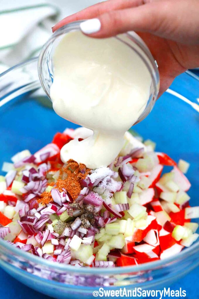 Adding mayo to the seafood salad in a bowl