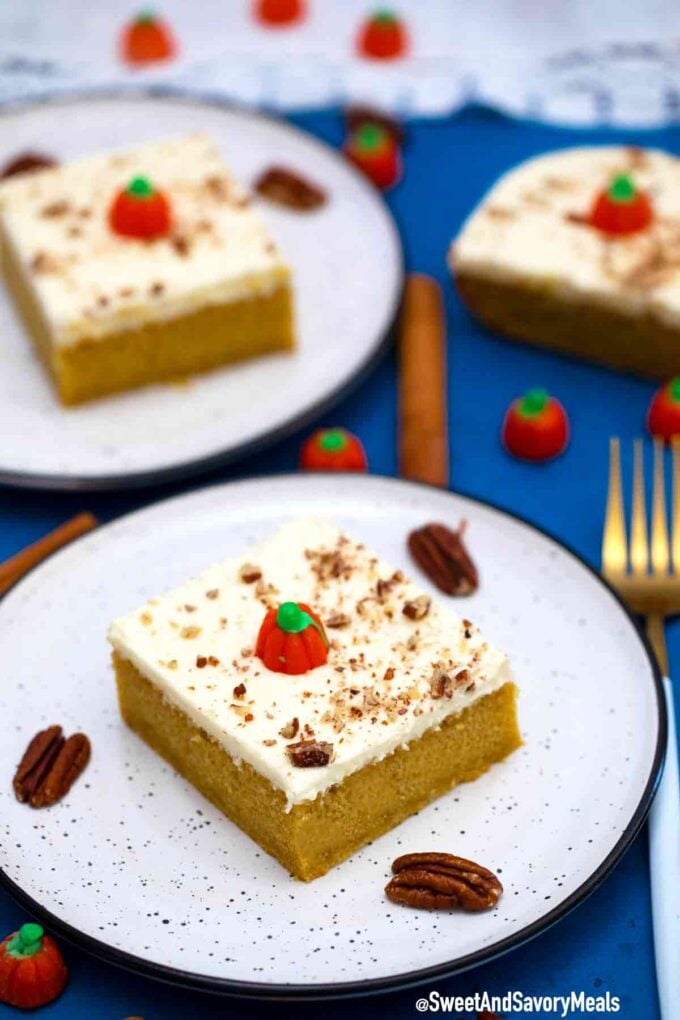 Pumpkin cake slice on a white plate next to some pecans 