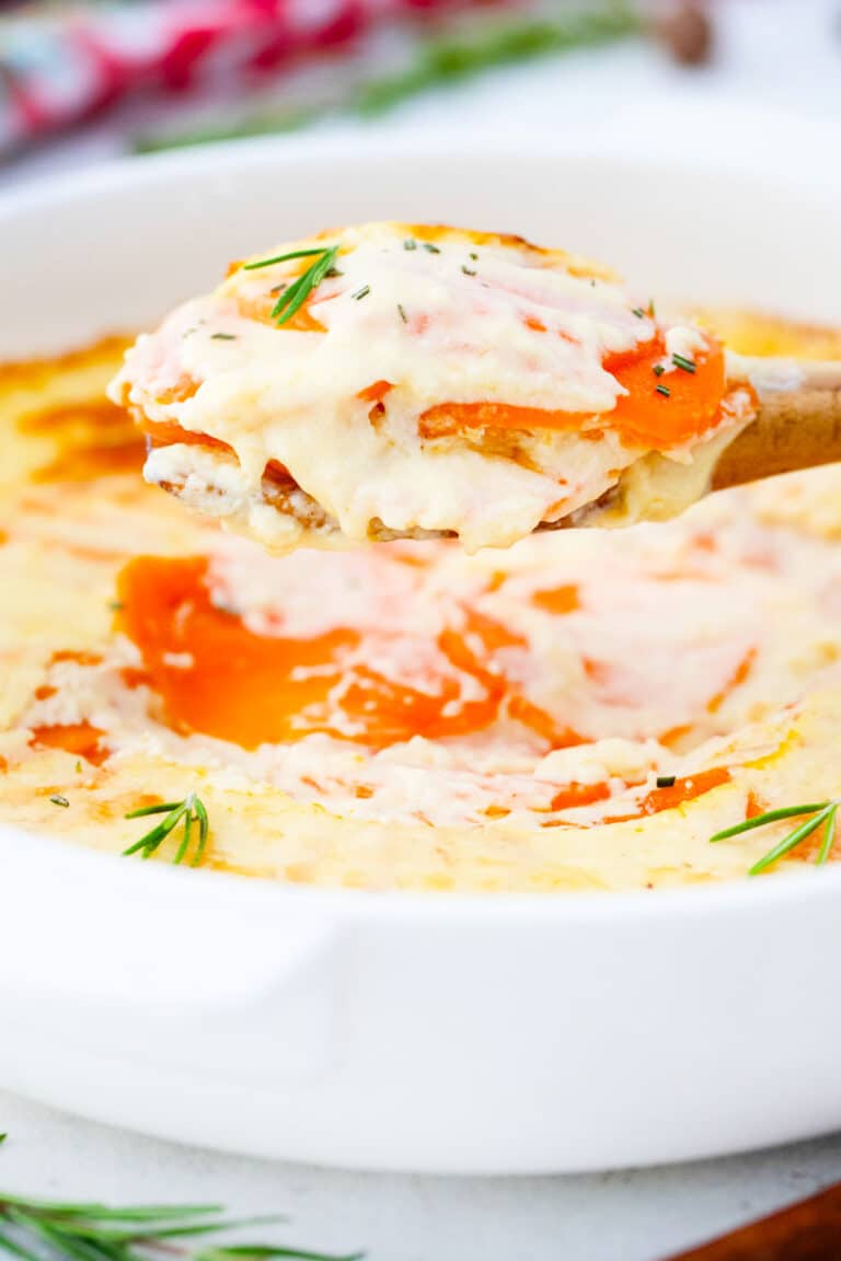 creamy and cheese scalloped sweet potatoes on a wooden spoon on top of a casserole dish