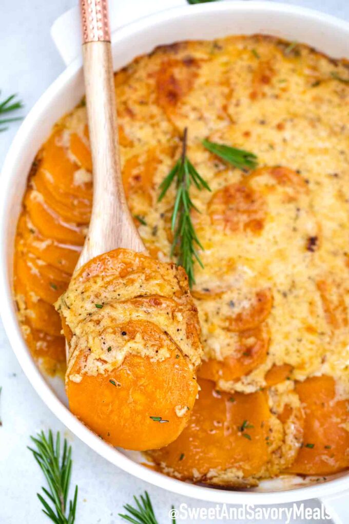 Scalloped sweet potatoes in a casserole dish and a wooden spoon