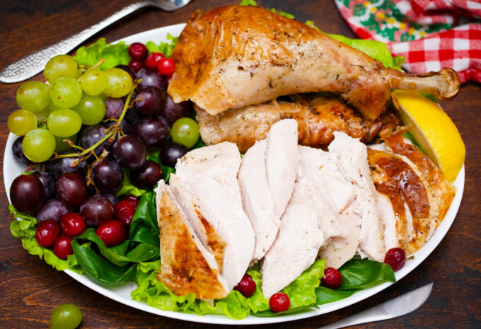 A plate of carved herb roasted turkey with grapes, cranberries, and greens.