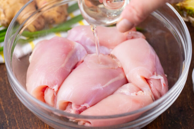 Drizzling canola oil over chicken pieces in a bowl.