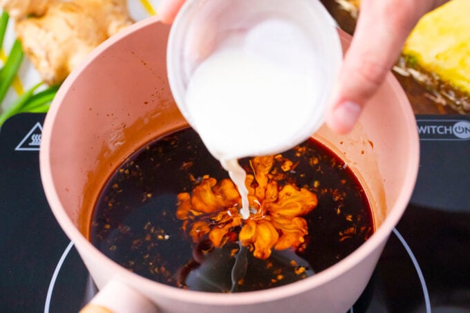 Adding cornstarch slurry to a saucepan with homemade teriyaki sauce.
