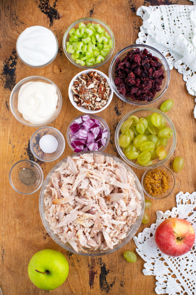 Overhead shot of turkey salad ingredients in bowls on a wooden table.