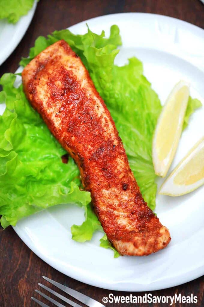 cooked and seasoned salmon fillet on a white plate with lettuce and sliced lemon