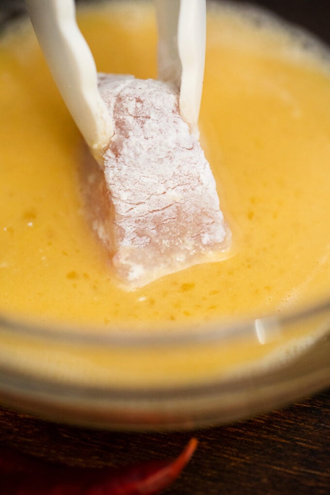 Dipping flour coated chicken pieces in beaten egg.