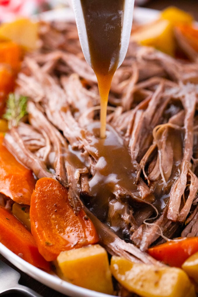 Pouring red wine glaze over crockpot red wine pot roast.