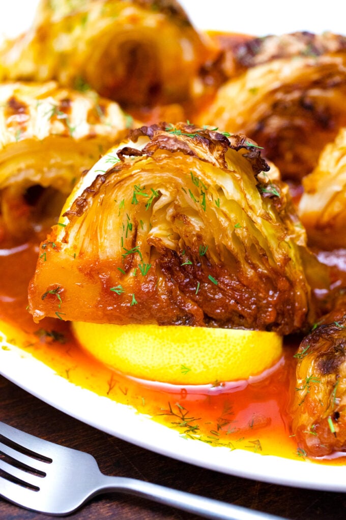 Caramelized cabbage wedges in tomato sauce served with lemon wedges.