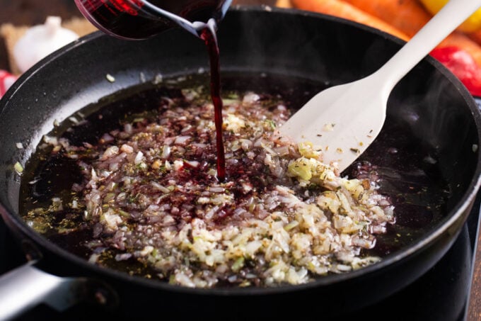 Adding red wine to a pan with onions and garlic.
