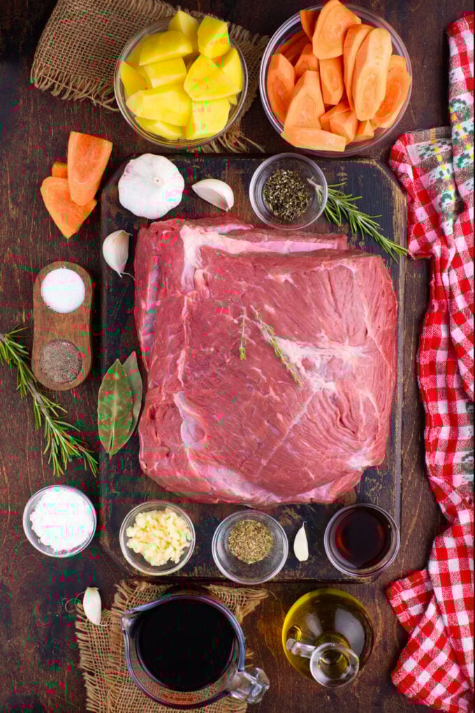 Overhead shot of slow cooker red wine pot roast ingredients arranged on a wooden table.