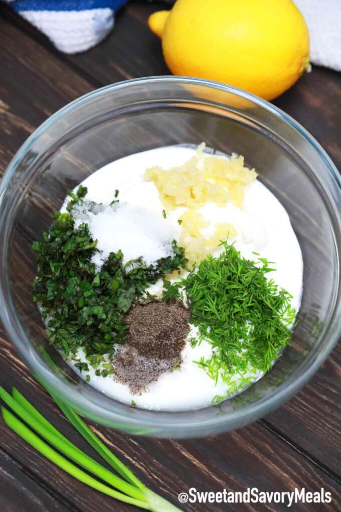 yogurt sauce ingredients in a large bowl on a table next to a lemon