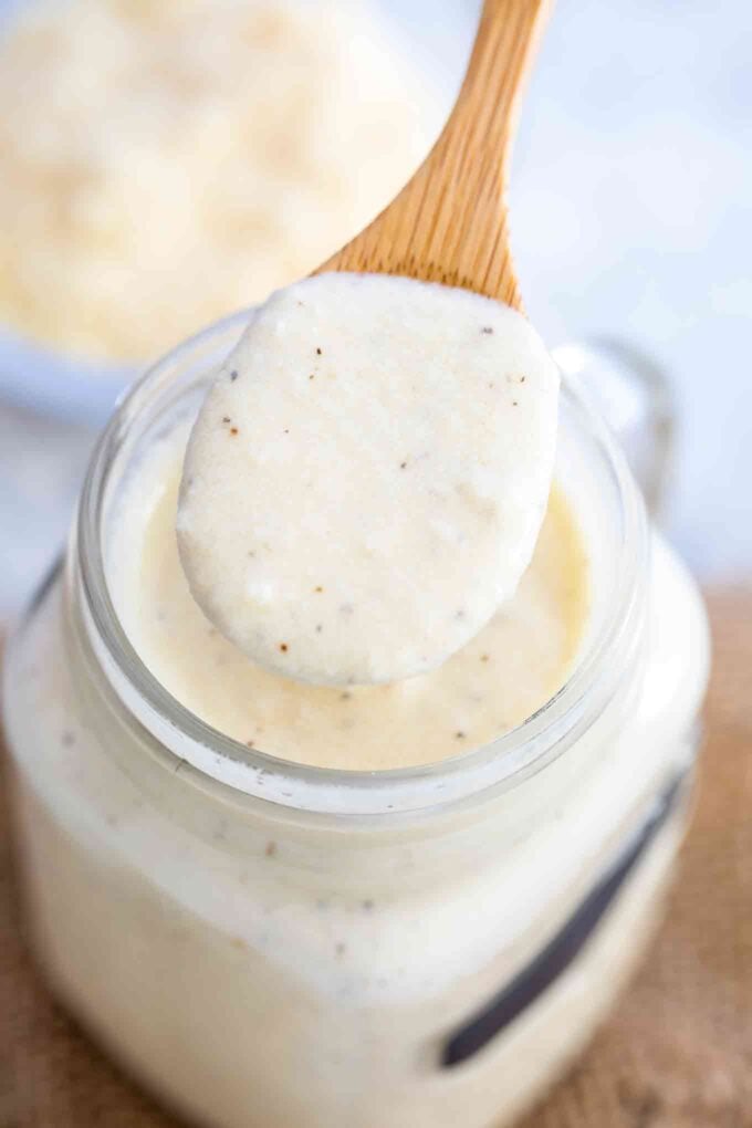 Alfredo Sauce on a wooden spoon on top of a jar with sauce