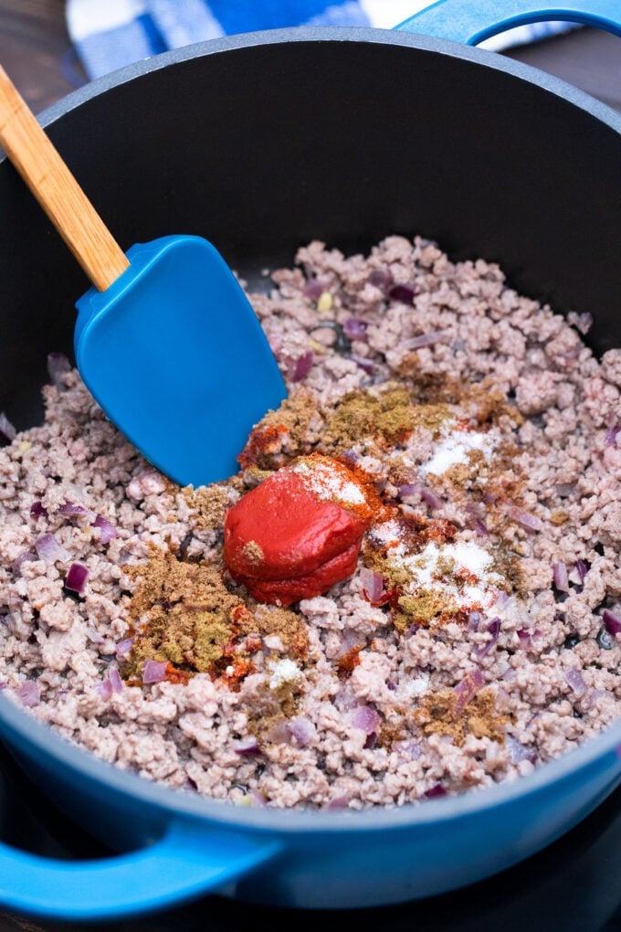 Adding spices and tomato paste to a pot with ground beef.