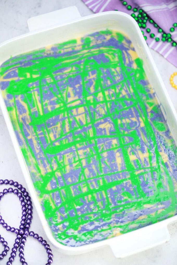 Green, purple, and yellow, batter swirls in a baking pan.