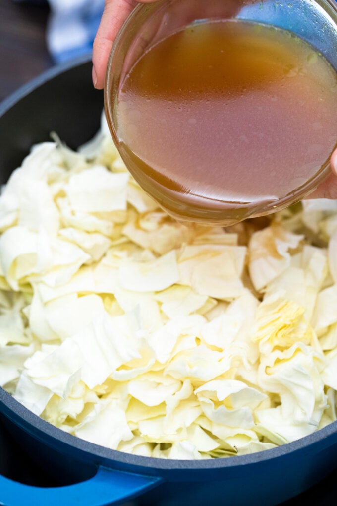 Pouring beef broth over chopped cabbage.