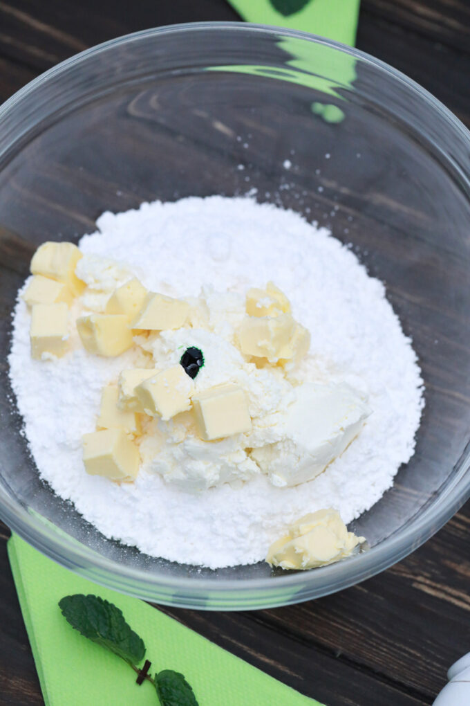Powdered sugar, butter, and green gel food coloring in a bowl.