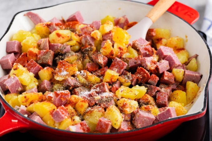 Adding cubed corned beef and seasonings to corned beef hash.