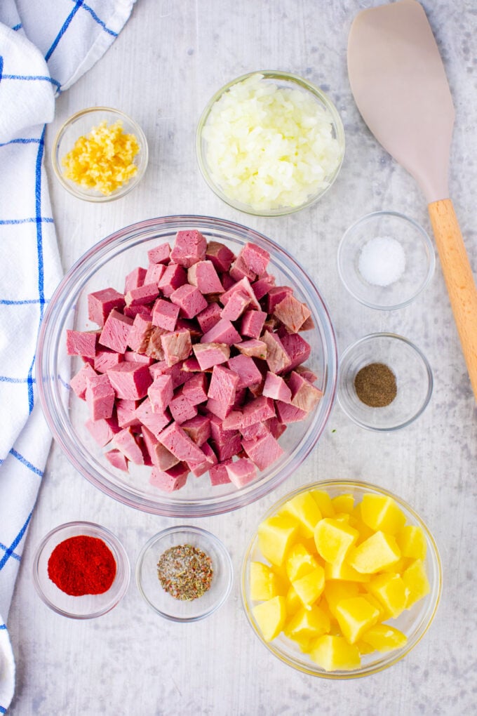 Overhead shot of corned beef hash ingredients in bowls on a light surface.