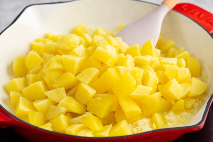 Adding cubed potatoes to a skillet.