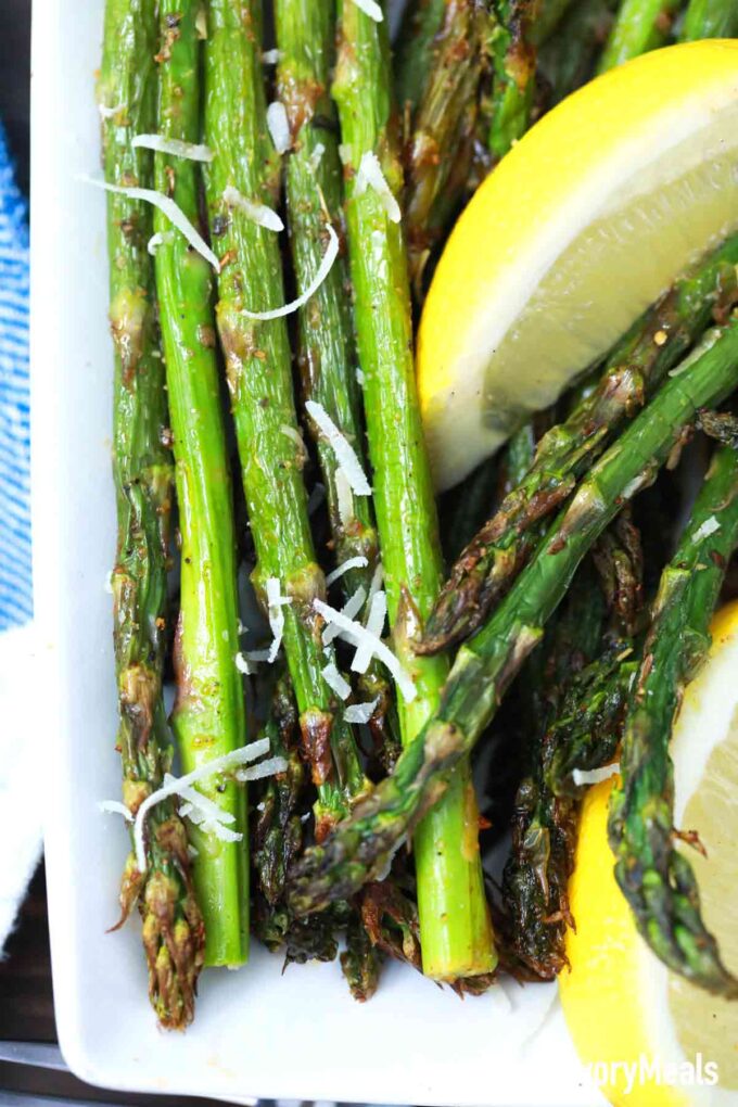 crispy asparagus with shredded cheeses on top and slice of lemon on a white plate