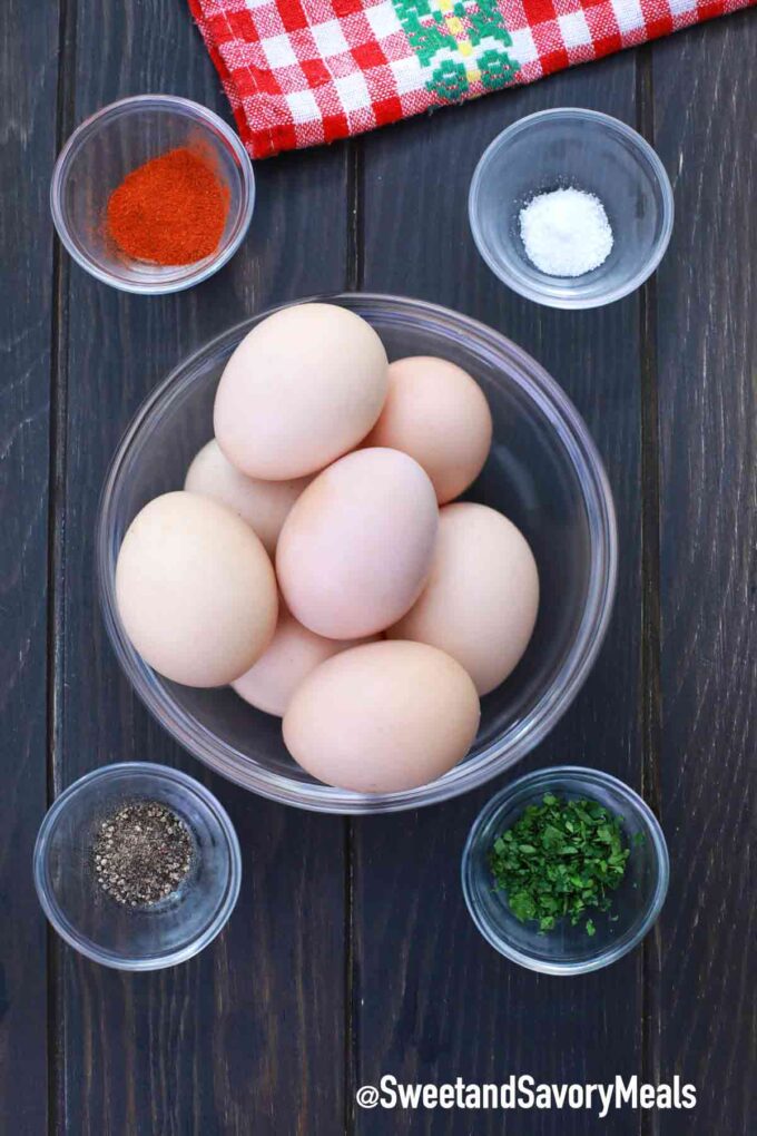 A dozen of white eggs along with paprika, black pepper, salt, and chopped parsley on a wooden board. 