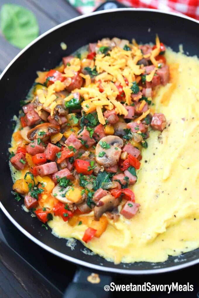 omelet in a skillet with veggies meat and cheese