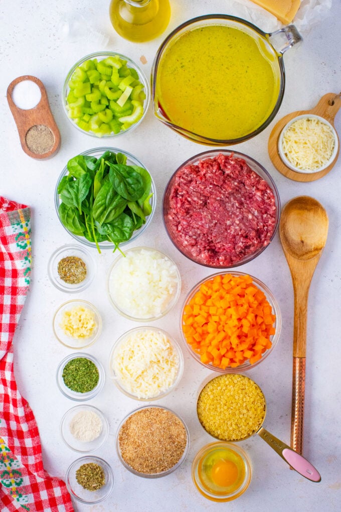 Overhead shot of slow cooker Italian wedding soup ingredients in bowls on a white surface.