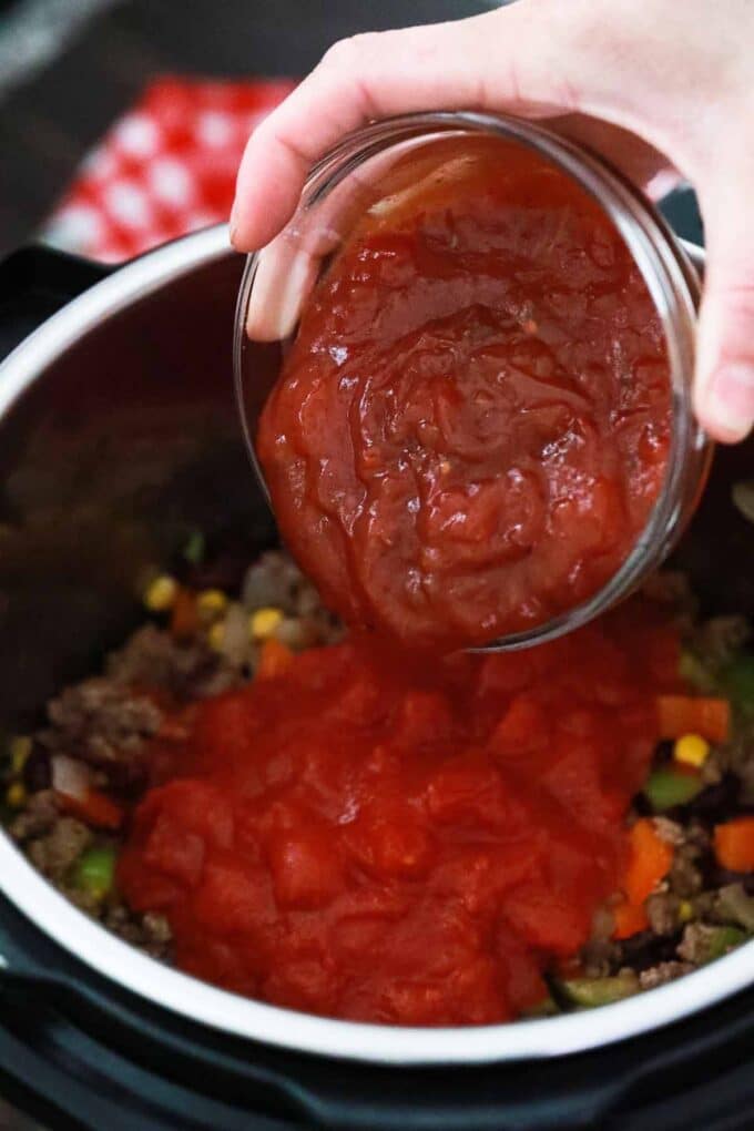 Adding salsa to Instant Pot Mexican casserole ingredients in the instant pot.