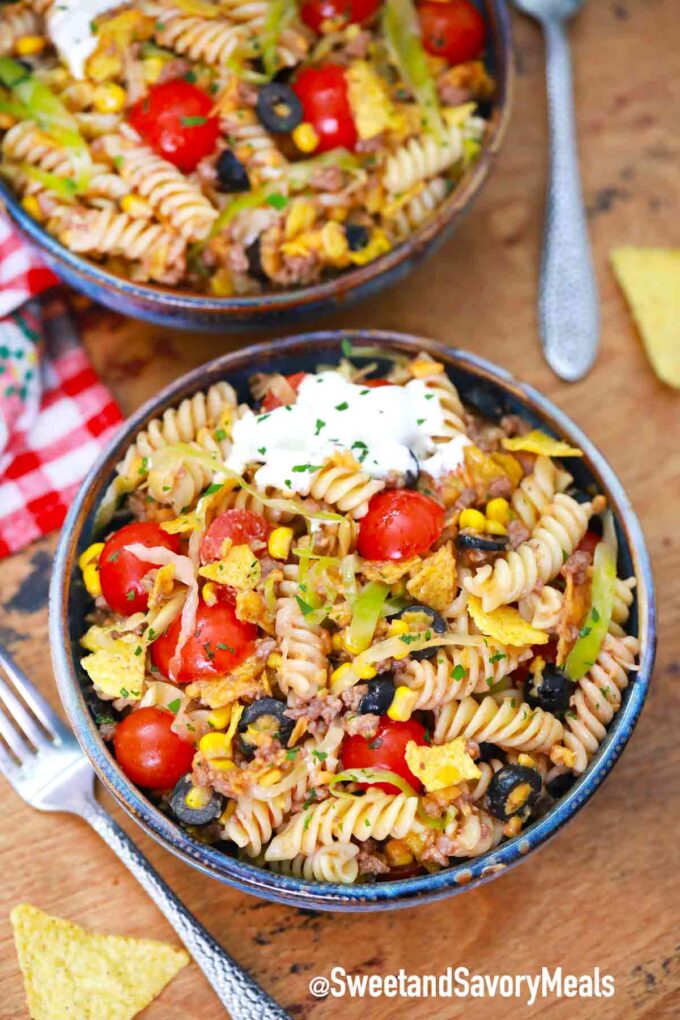 two bowls of taco pasta salad topped with sour cream and cheese on a table.