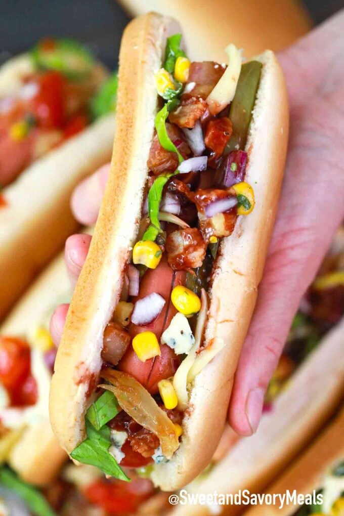 hot dog topped with corn and red onion held in a palm