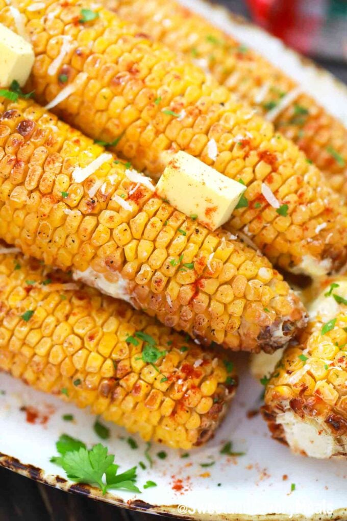 air fried corn on the cob on a platter toped with shredded cheese and butter
